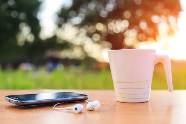 Taza de café y teléfono inteligente en la mesa en la hora del atardecer — Foto de Stock