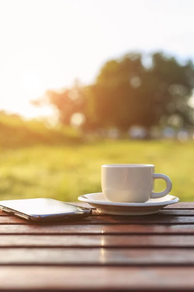 Taza de café y teléfono inteligente en la mesa en la hora del atardecer — Foto de Stock