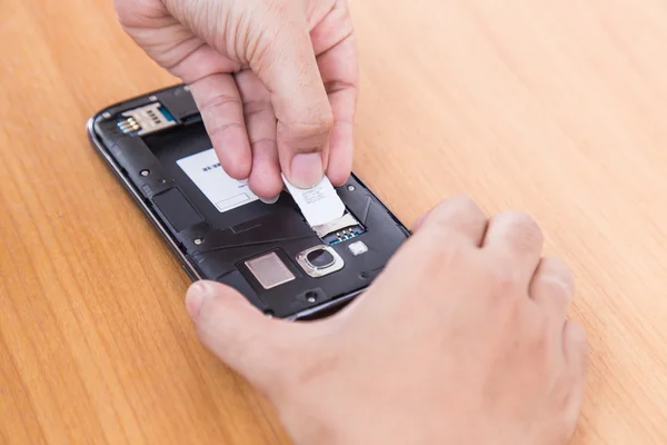 La celebración de la mano tarjeta SIm y teléfono inteligente sobre fondo de madera — Foto de Stock