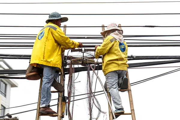 Dos trabajadores masculinos en escalera de bambú están reparando la línea telefónica cerca de la comunidad el 20 de agosto de 2014 en Phuket Tailandia . —  Fotos de Stock