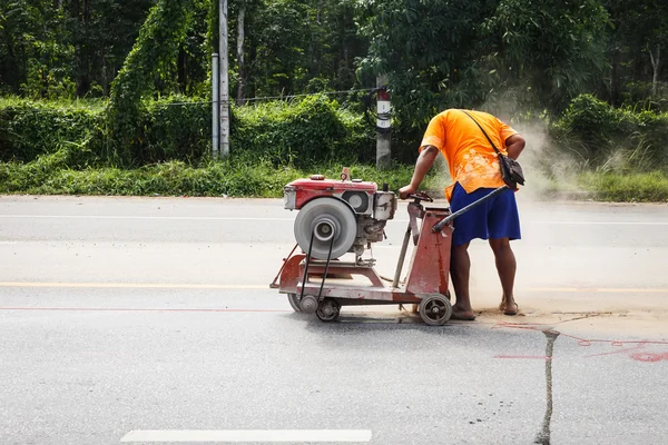 Резание асфальтовой дороги для ремонта с помощью гидравлической угловой шлифовальной машины — стоковое фото