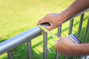 Man measuring stainless steel railing with measuring tape. clipart