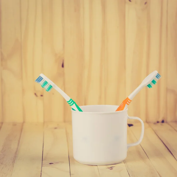 Toothbrushes in cup on wooden table — Stock Photo, Image