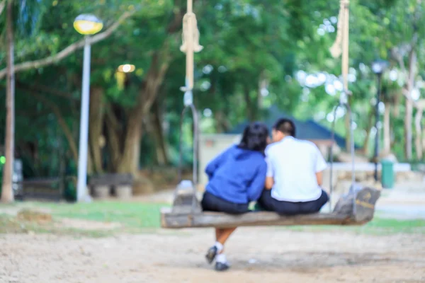 Garçon et fille en uniforme étudiant assis sur swing — Photo