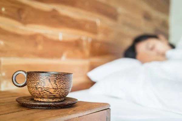 Taza de café en la mesa y la mujer en la cama — Foto de Stock