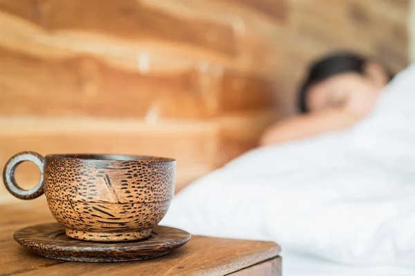 Taza de café en la mesa y la mujer en la cama — Foto de Stock