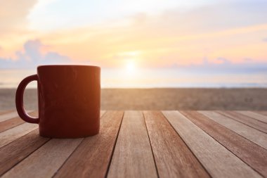 Coffee cup on wood table at sunset or sunrise beach clipart