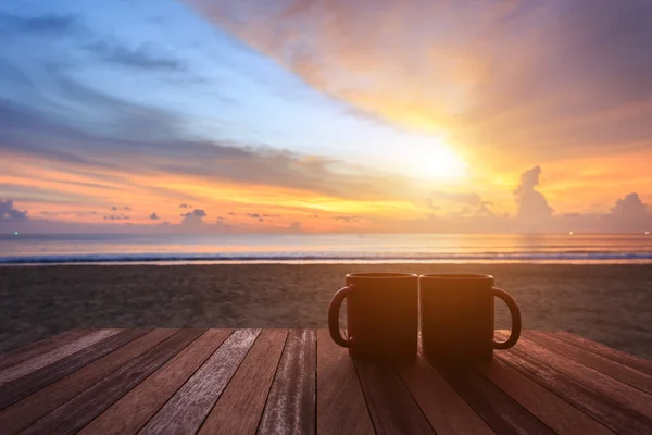 Kahve fincanı gündoğumu veya günbatımı Plajı'nda ahşap masa üzerinde — Stok fotoğraf