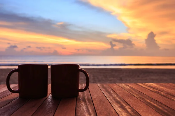 Coffee cup on wood table at sunset or sunrise beach — Stock Photo, Image