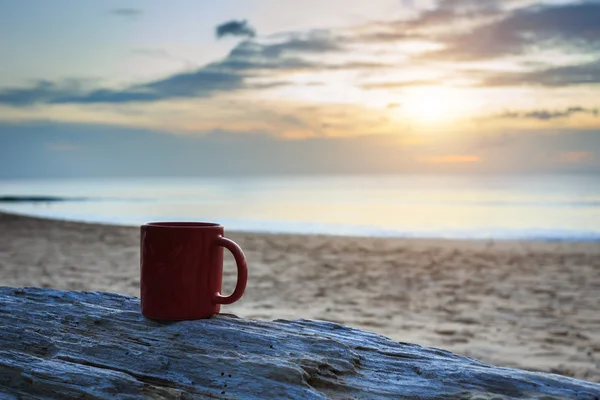 Coffee cup on wood log at sunset or sunrise beach — Stock Photo, Image
