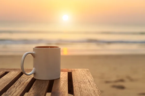 Cangkir kopi di atas meja kayu saat matahari terbenam atau pantai terbit — Stok Foto