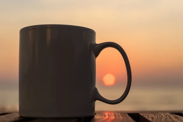 Чашка кави на дерев'яному столі на заході сонця або східному пляжі — стокове фото