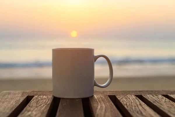 Filiżanka kawy na stół z drewna na zachód lub wschód słońca plaży — Zdjęcie stockowe