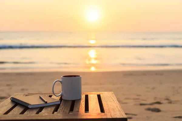 Coffee cup on wood table at sunset or sunrise beach