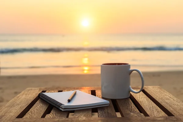 Xícara de café na mesa de madeira ao pôr do sol ou ao nascer do sol praia — Fotografia de Stock