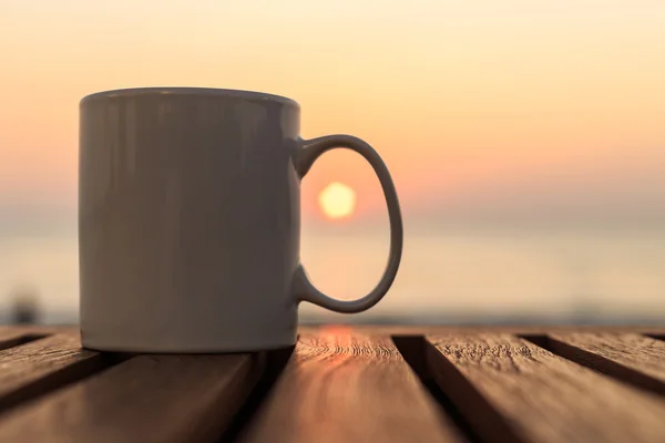 Koffiekopje op houten tafel bij zonsondergang of zonsopgang strand — Stockfoto