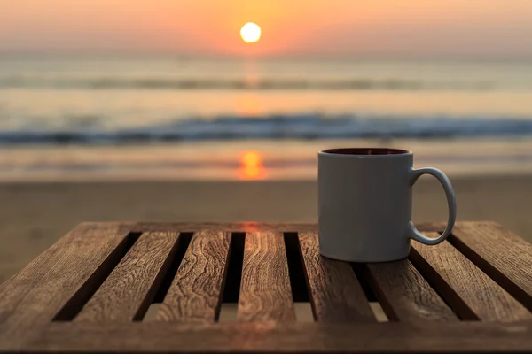 夕日や日の出のビーチで木製テーブルの上のコーヒー カップ — ストック写真