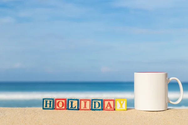 Palabra HOLIDAY en bloques de alfabeto de colores y taza de café en tropi — Foto de Stock