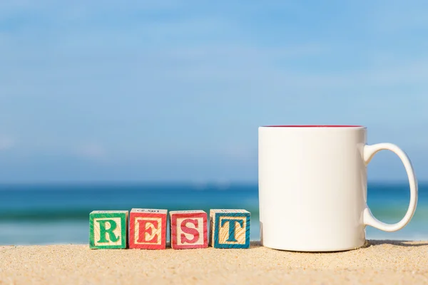 Word REST in colorful alphabet blocks and coffee cup on tropical — Stock Photo, Image