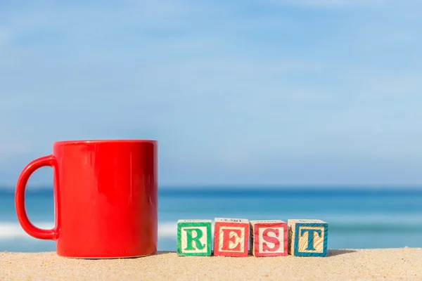 Word REST in colorful alphabet blocks and coffee cup on tropical — Stock Photo, Image