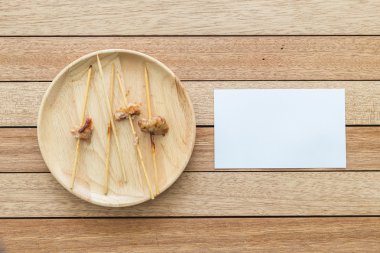 Empty bamboo stick of grilled pork and paper note on wooden dish
