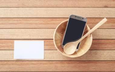 Top view smartphone in wooden bowl on wooden plank background