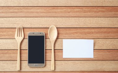Top view smartphone, spoon and fork on wooden plank background