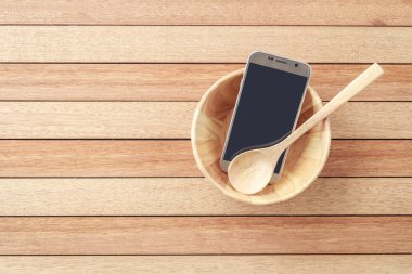 Top view smartphone in wooden bowl on wooden plank background