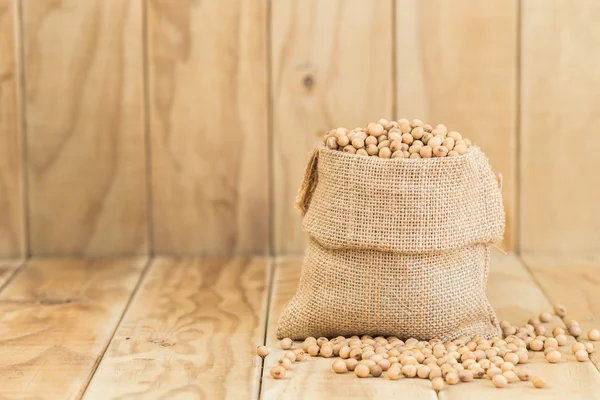 Soy beans in sack on wooden desk — Stock Photo, Image