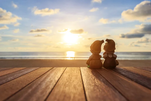 Dos muñecas sentadas en una mesa de madera en la playa al atardecer — Foto de Stock