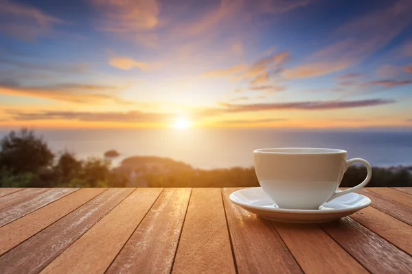 Taza de café blanco en la mesa de madera y vista de la puesta del sol o la salida del sol bac — Foto de Stock