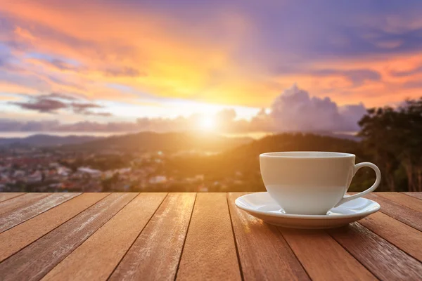 Vit kaffekopp på bord av trä och utsikt över solnedgången eller sunrise bac — Stockfoto