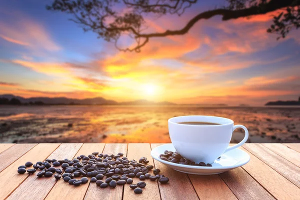 Weiße Kaffeetasse und Kaffeebohnen auf Holztisch und Blick auf Sonnen — Stockfoto