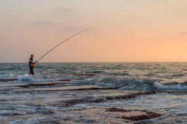 Hayfa, İsrail 08-07-2020 Adam gün batımında Hayfa, İsrail yakınlarındaki Akdeniz 'de balık tutuyor.