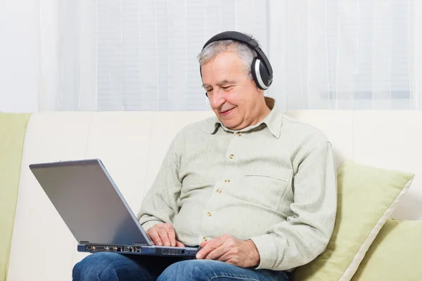 Uomo anziano con laptop e cuffie — Foto Stock