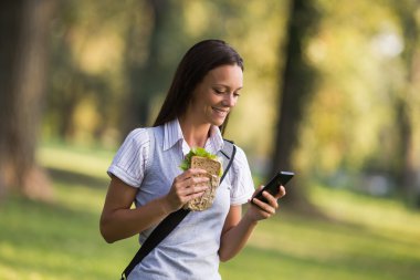 Sandviç yeme ve telefon kullanarak iş kadını