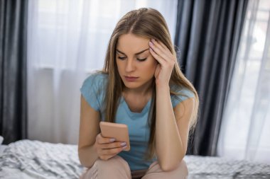 Yatak odasında yatarken telefonu tutan üzgün kadın..