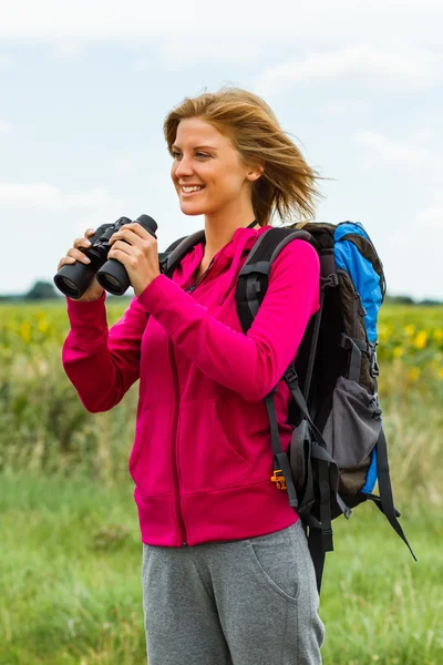 Woman with backpack and binoculars enjoys walking the country road — Stock Photo, Image
