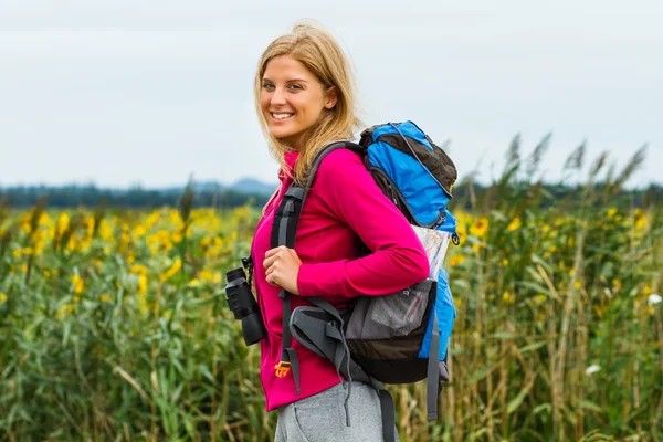 Mujer con mochila y binoculares disfruta paseando por el camino del campo —  Fotos de Stock