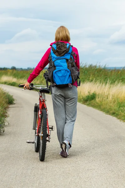 彼女の自転車の国の道路の上を歩く女性 — ストック写真