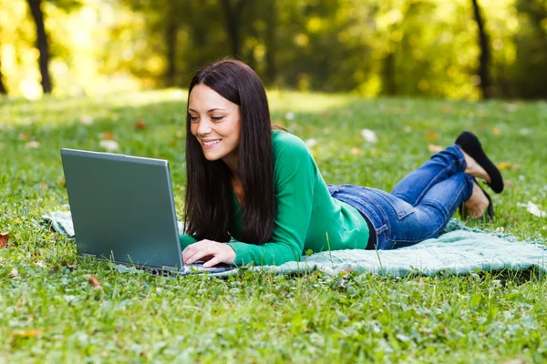 Vrouw is met behulp van haar laptop terwijl liggen in de natuur — Stockfoto