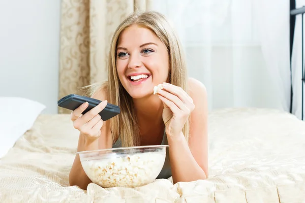 Mulher deitada na cama, comendo pipocas e assistindo tv — Fotografia de Stock