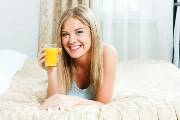 Woman lying on her bed and drinking orange juice — Stock Photo, Image