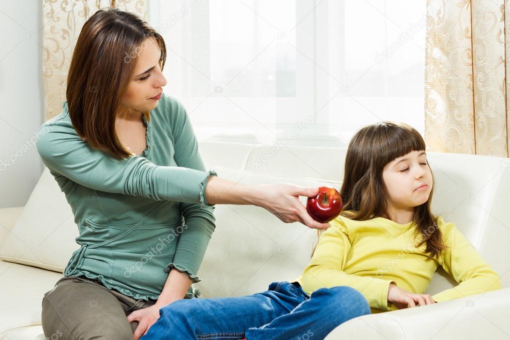 Mother is giving apple to her angry daughter