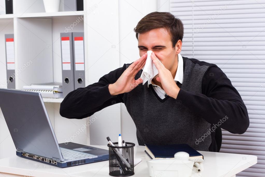 Businessman sneezing while working