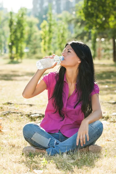 女人坐在公园和饮用水 — 图库照片
