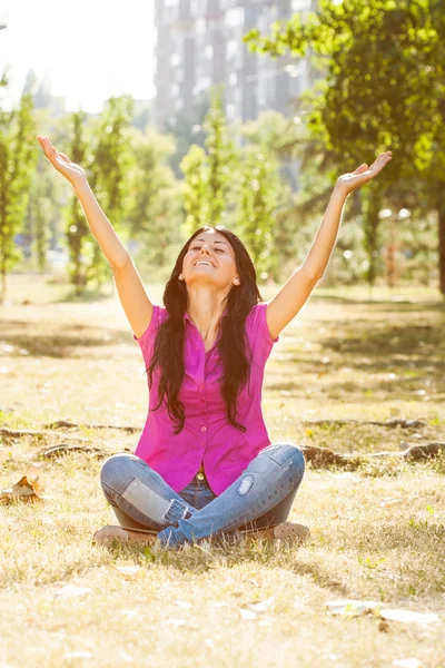 Woman is sitting in the park with her arms outstretched — Stock Photo, Image