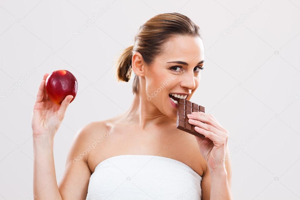 Woman biting chocolate and holding apple