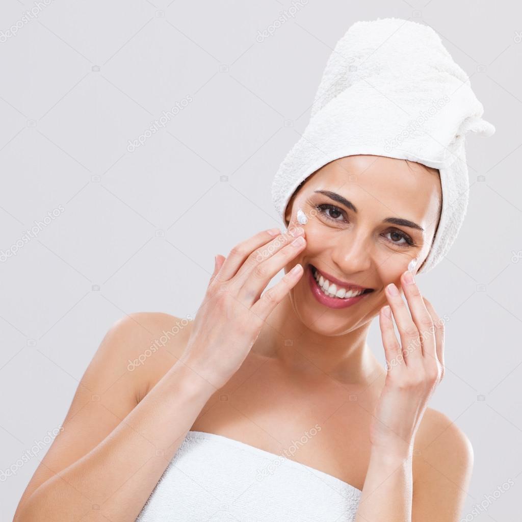 Woman is applying lotion on her face