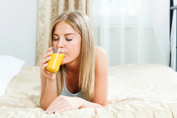 Žena leží na posteli a pít pomerančový džus — Stock fotografie